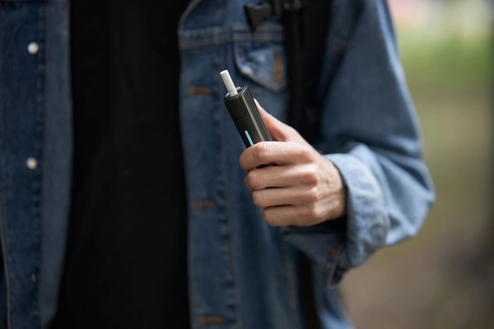 Pessoa jovem segurando com a mão esquerda um cigarro eletrônico, popularmente conhecido como vape.